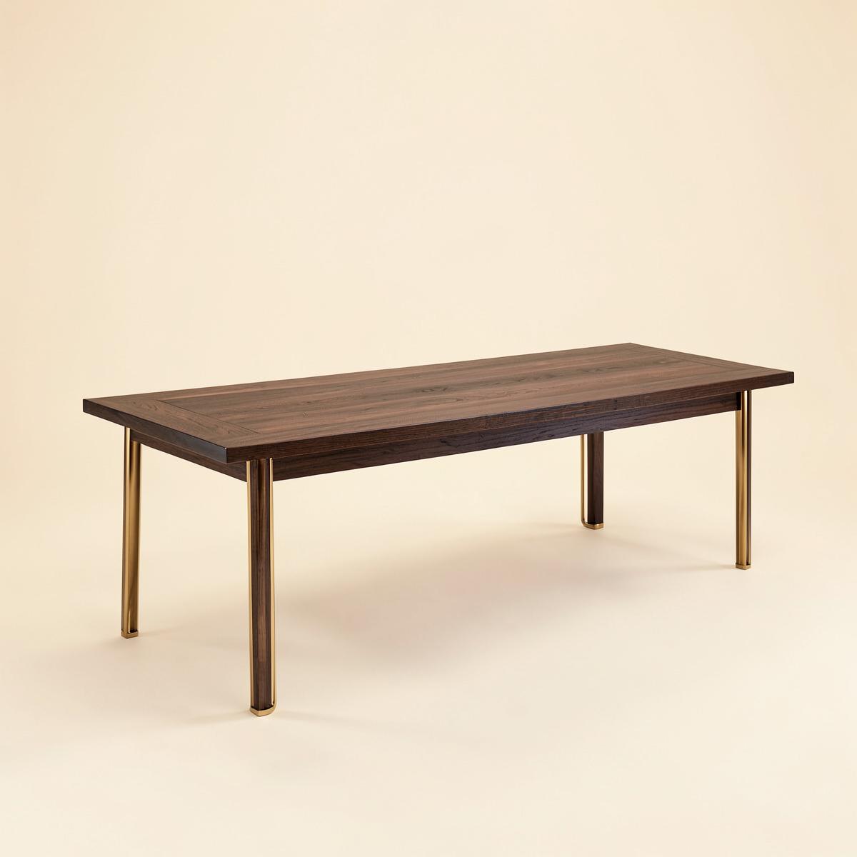 Long dark-stained oak dining table with slim brass leg details on a plain background